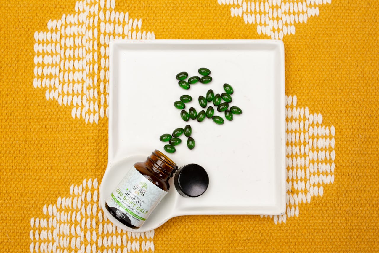 CBD oil capsules in a bottle on a white tray over an orange patterned fabric. Ideal for health and wellness themes.