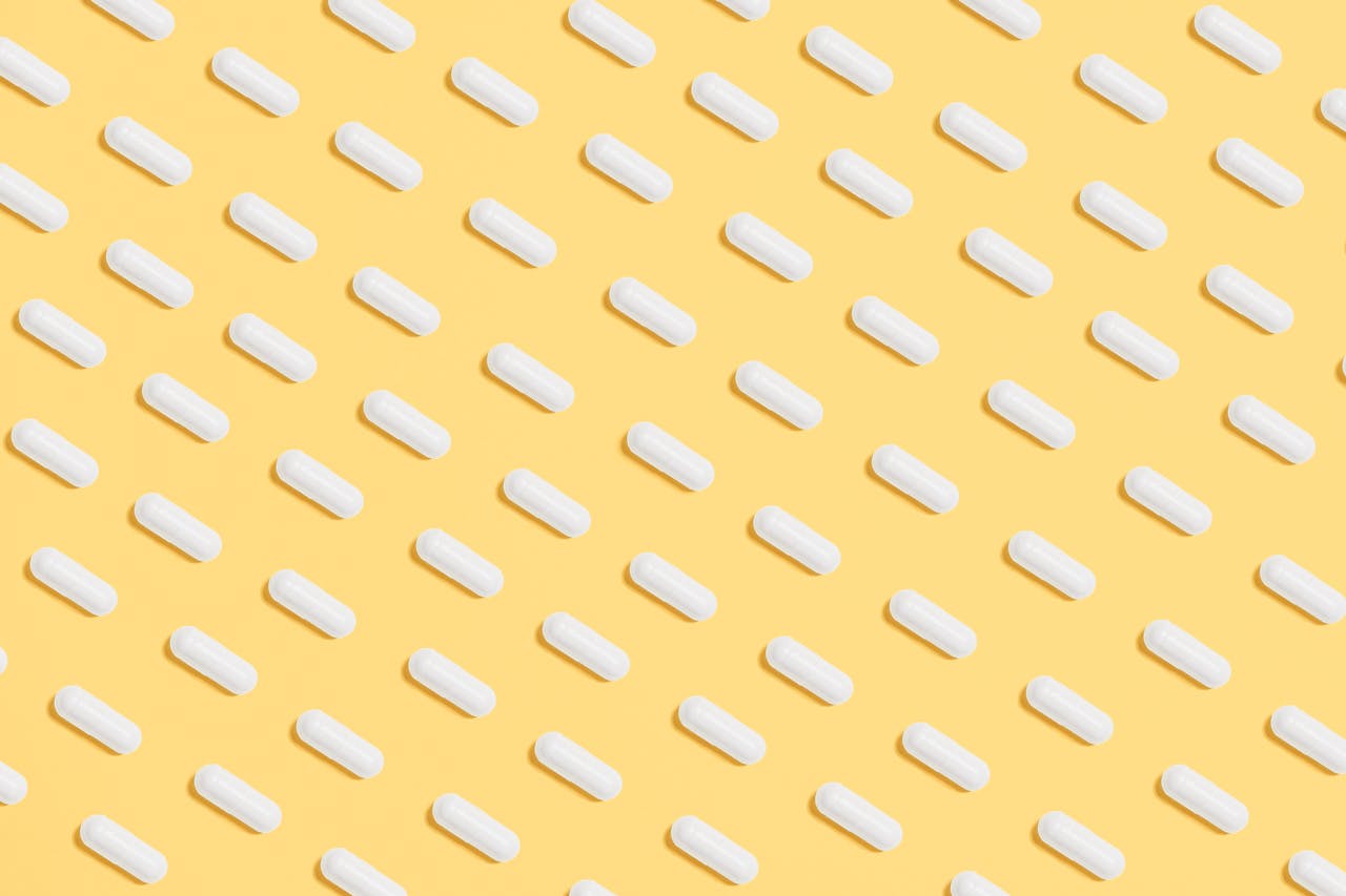 Pattern of white capsules on a bright yellow surface, symbolizing healthcare and medicine.