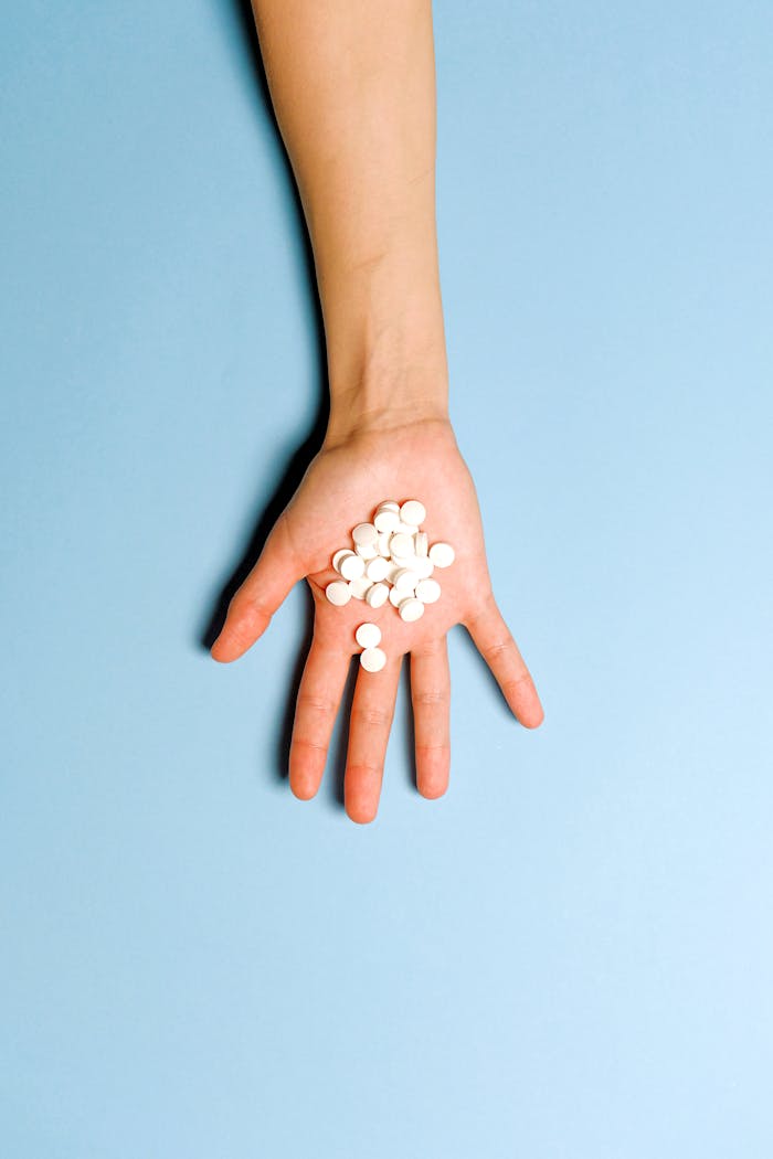 A hand holding white pills on a light blue background symbolizing medication and healthcare.