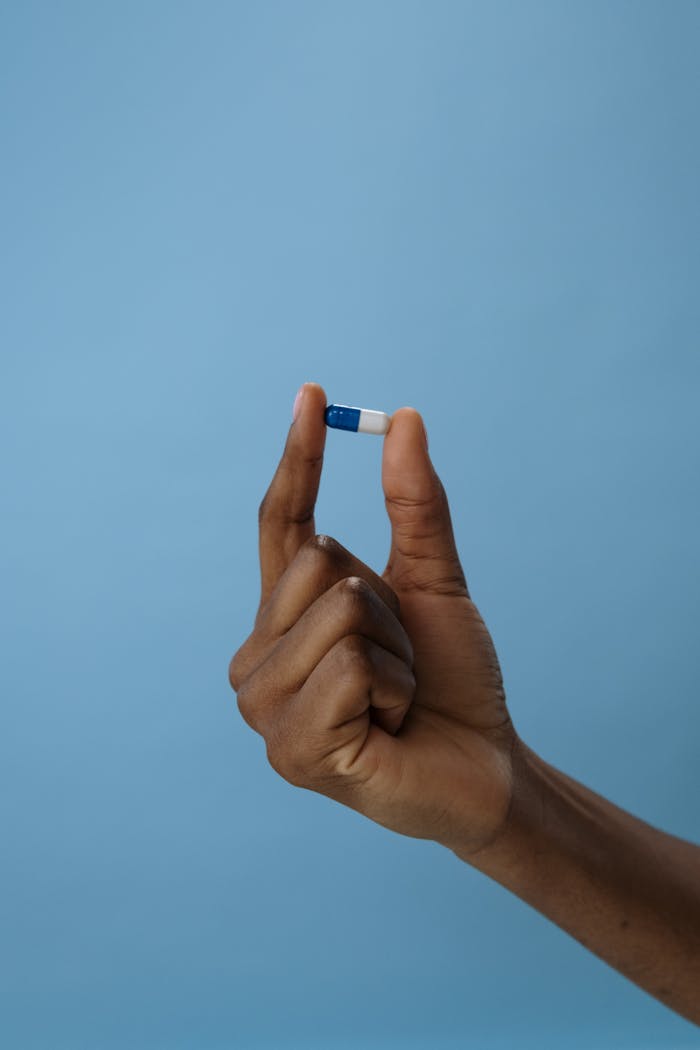 Close-up of a hand holding a blue and white capsule against a plain background. Ideal for medical themes.