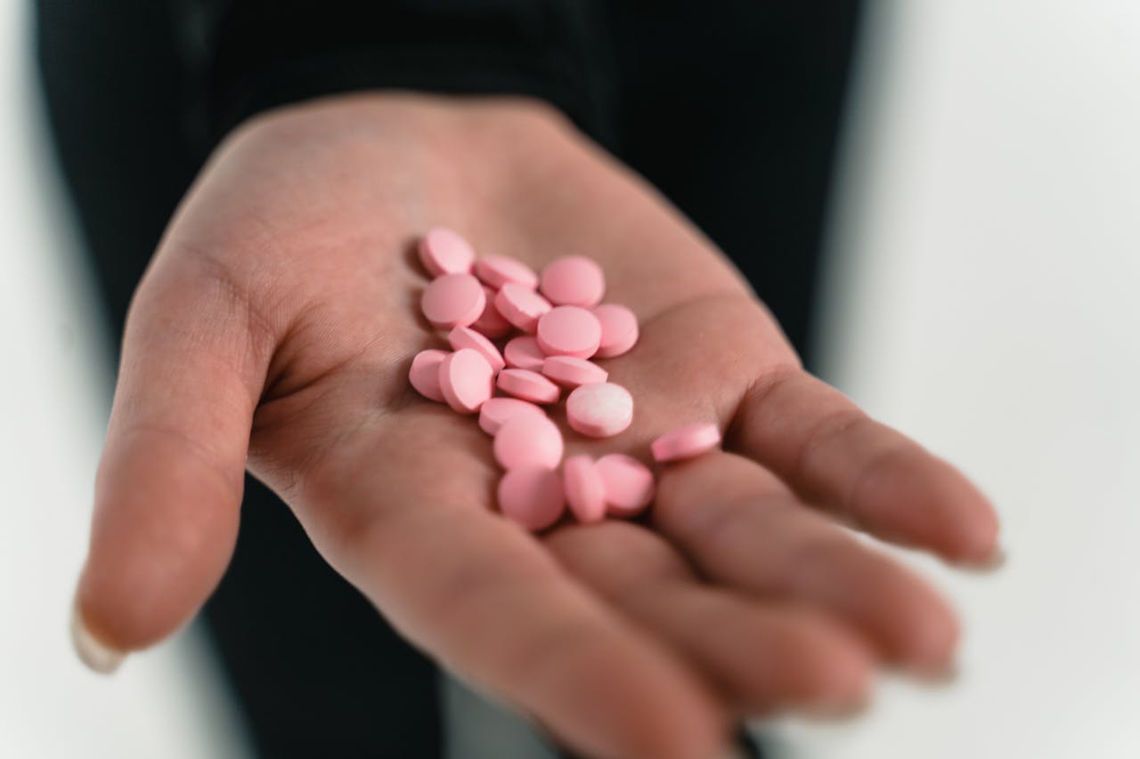 A close-up of a hand holding pink pills, highlighting healthcare concepts.